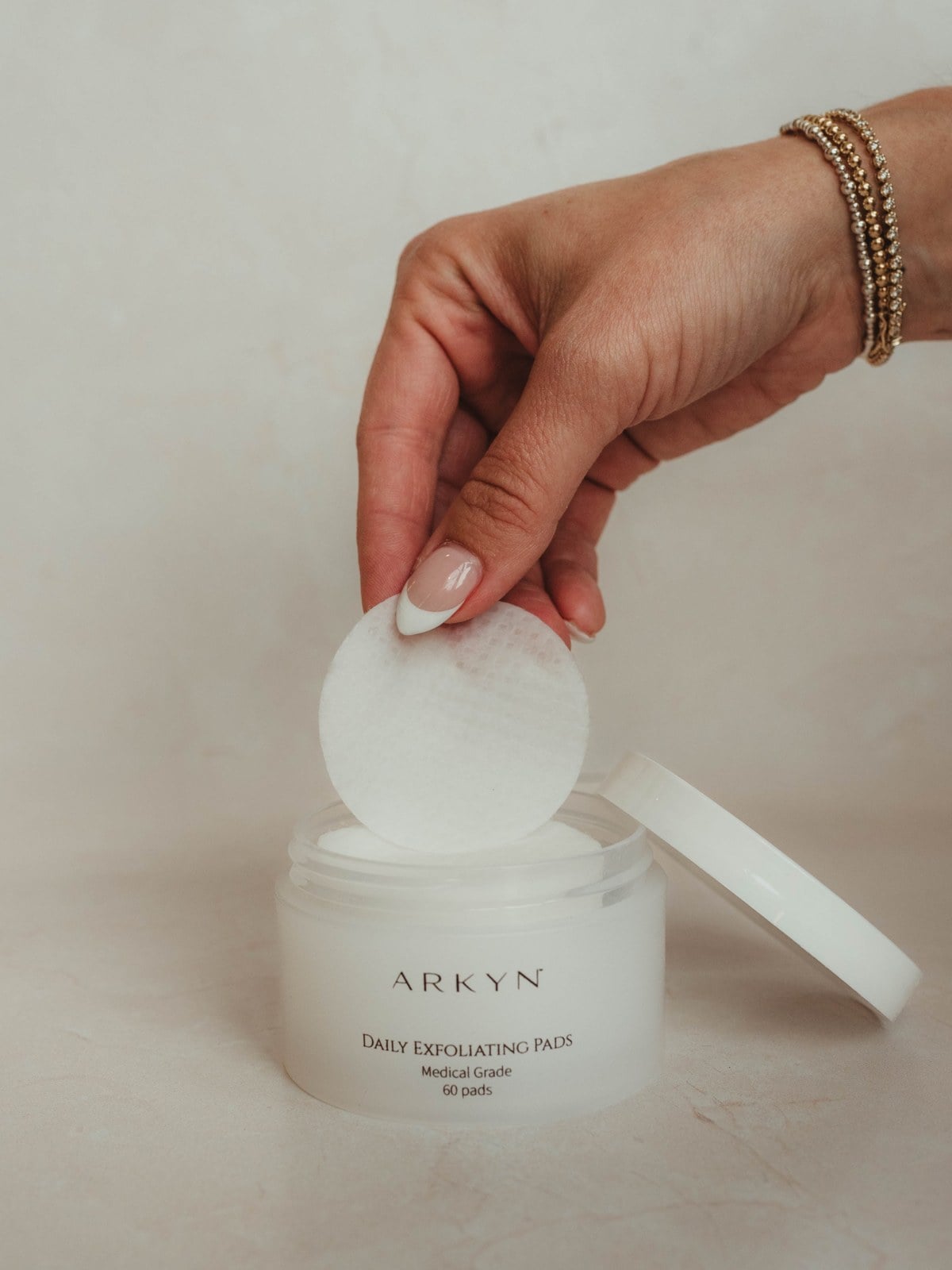 A hand lifting an exfoliating pad from the Arkyn jar
