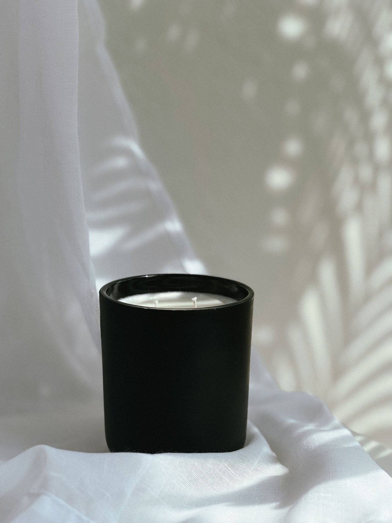 The Boldly Her candle in a black vessel, photographed against a linen backdrop