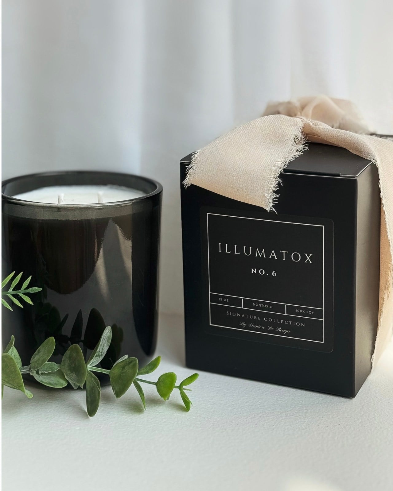 A lit Illumatox candle beside its black gift box with a cream ribbon