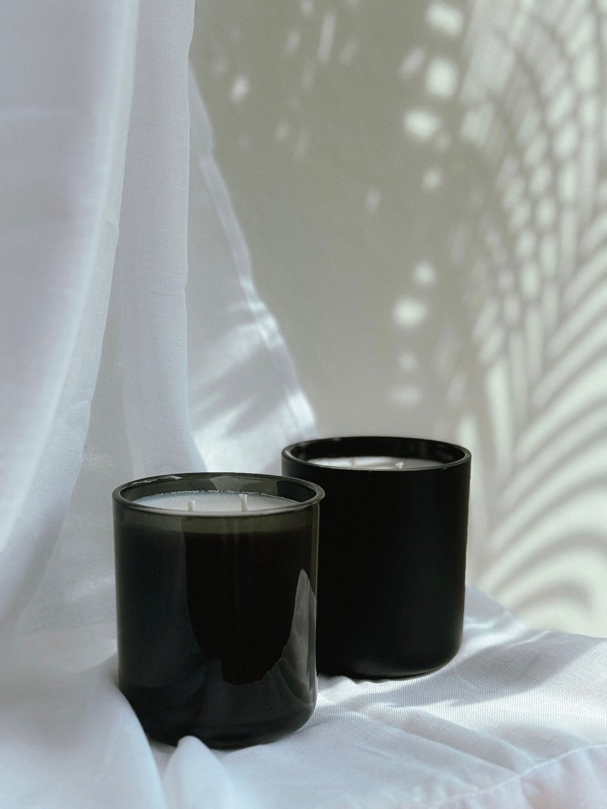Two Illumatox candles in black vessels photographed against linen