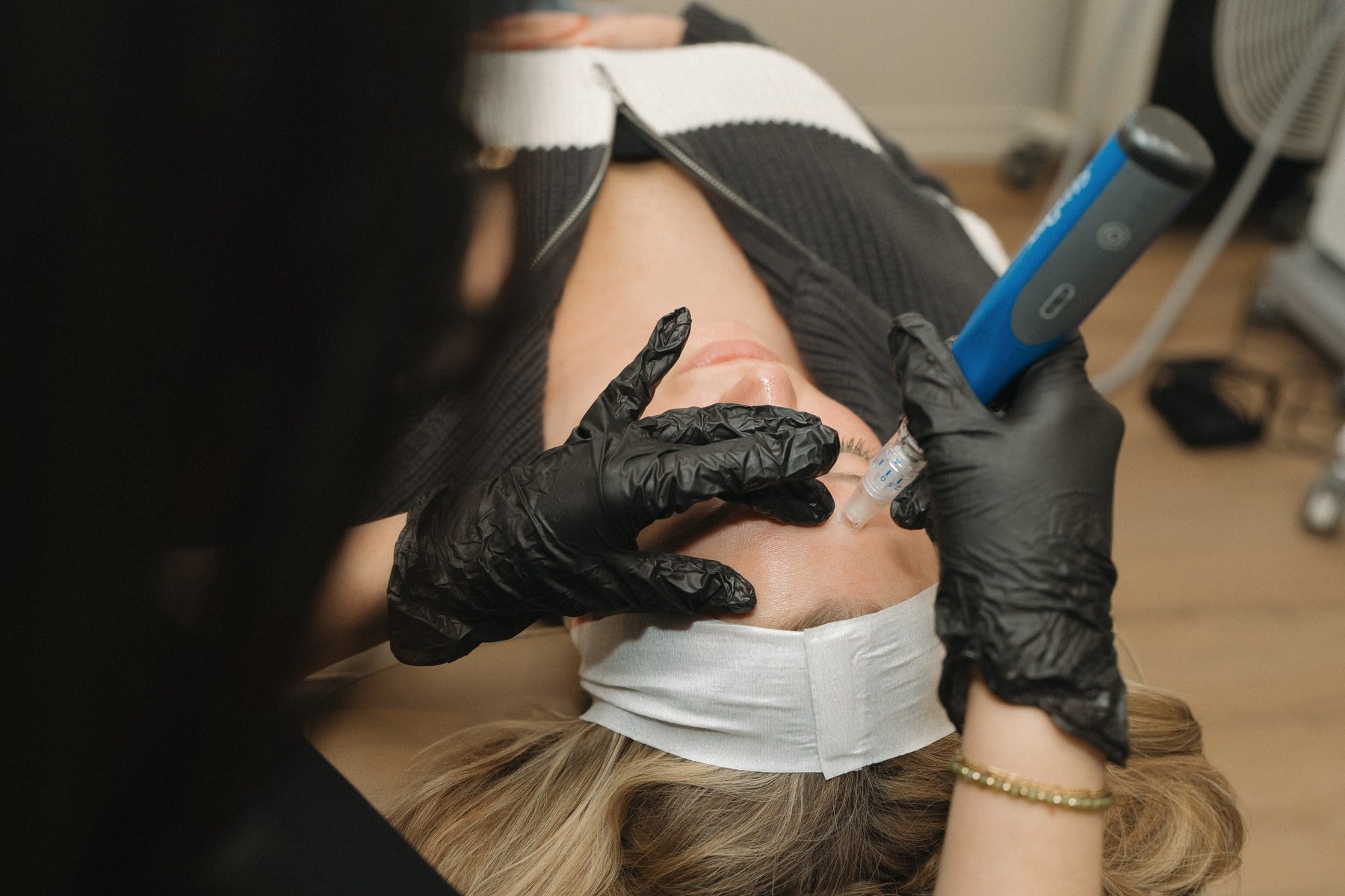 A laser handpiece with a blue tip being passed over a reclined client's cheek at Illumatox in Neenah