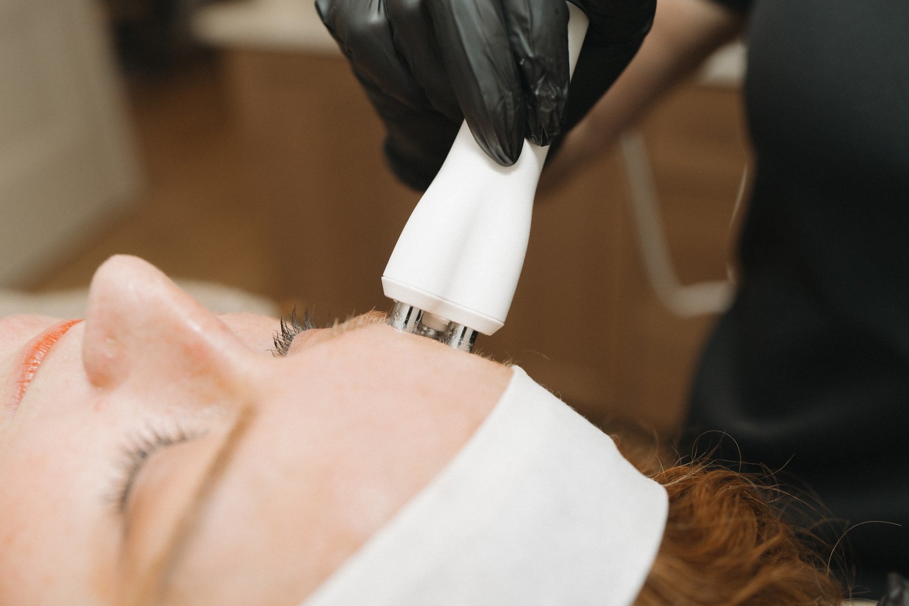 A skin treatment handpiece being passed across a client's cheek at Illumatox in Neenah